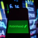 This photo illustration shows a Robinhood logo is displayed on a smartphone with stock market percentages on the background.