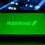 A Robinhood logo seen displayed on a smartphone with the stock market graphic in the background.
